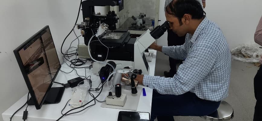 A trainee working at a microscope with a display screen